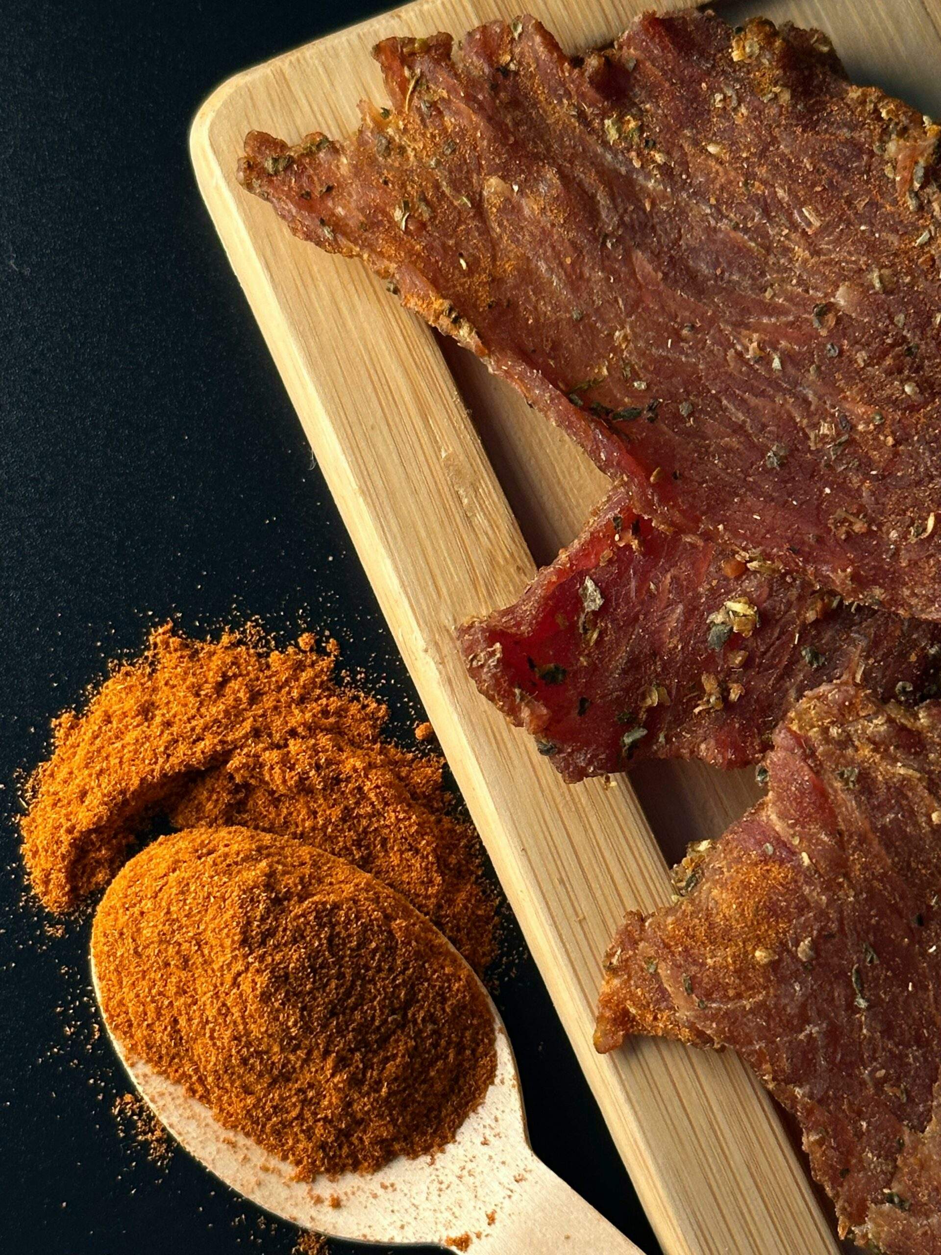 Home Close-up of savory beef jerky slices with a spicy powder on a wooden spoon creating a flavorful combination.