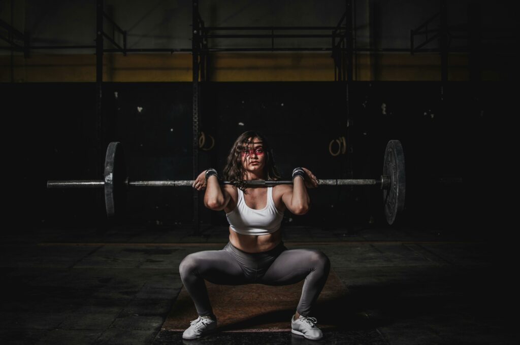 Home A strong female weightlifter squats with a barbell in a dimly lit gym, showcasing power and fitness.